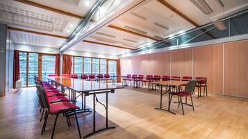 A conference room with a long table and red chairs, large windows, and wooden paneling.