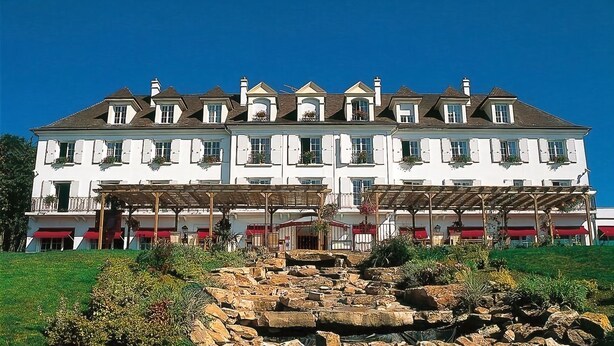 A large white building with multiple balconies and a stone fountain in the foreground.