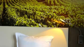 Habitación de hotel con cama, almohadas blancas y una lámpara fijada a la pared.