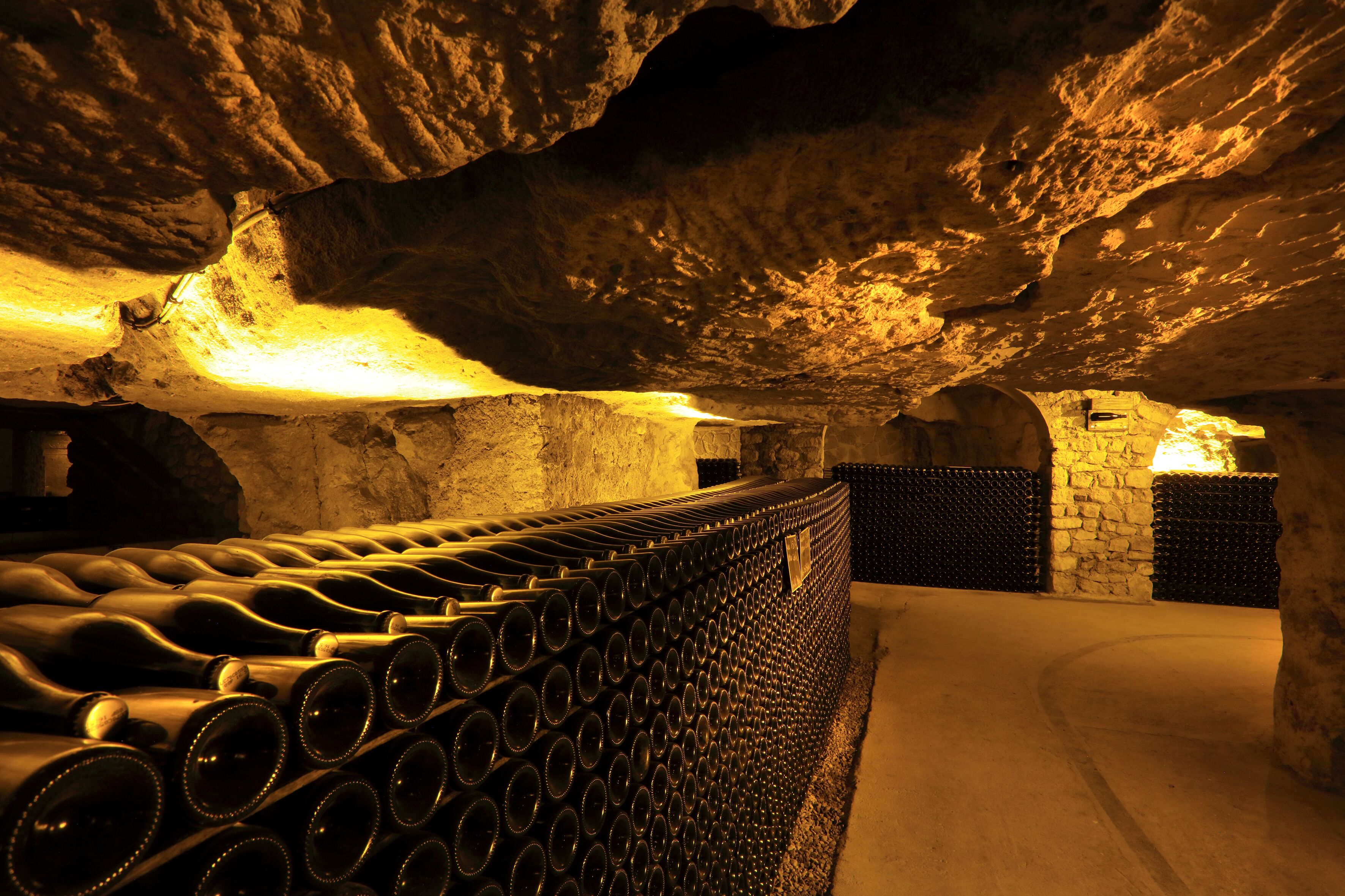 Un interior que recuerda a una cueva, con una fila de botellas de vino y paredes de piedra.
