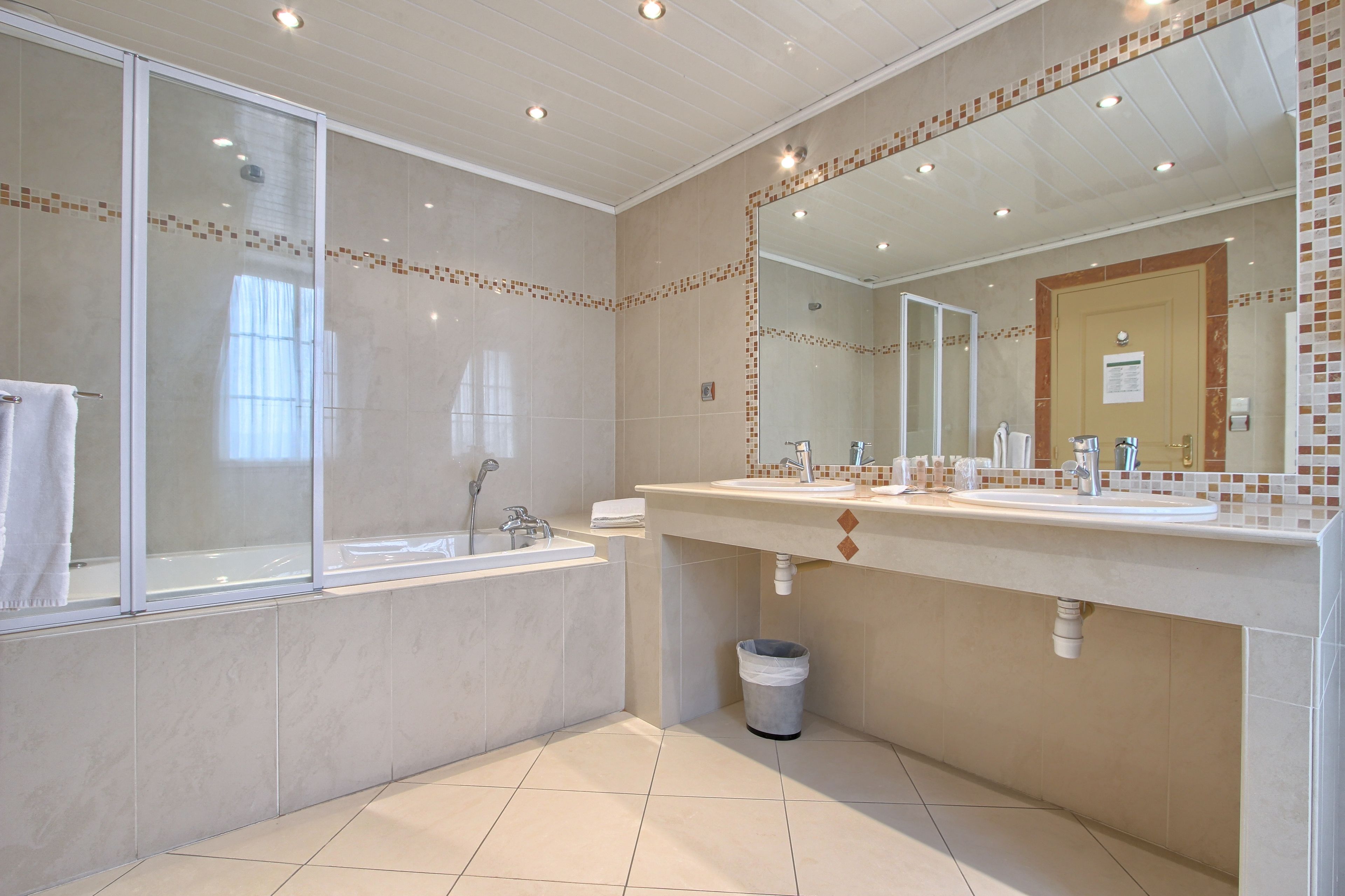 A modern bathroom with a large bathtub, a vanity with a mirror, and a trash can.