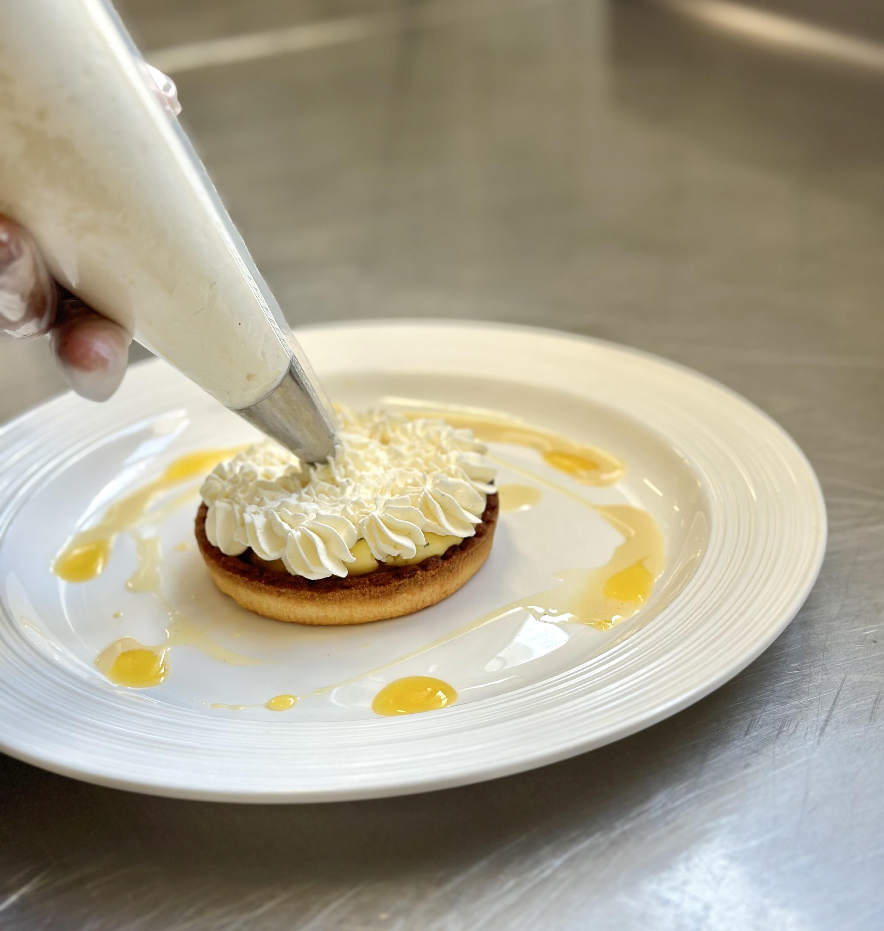 Un dessert est décoré avec de la crème à l’aide d’une poche à douille sur une assiette.