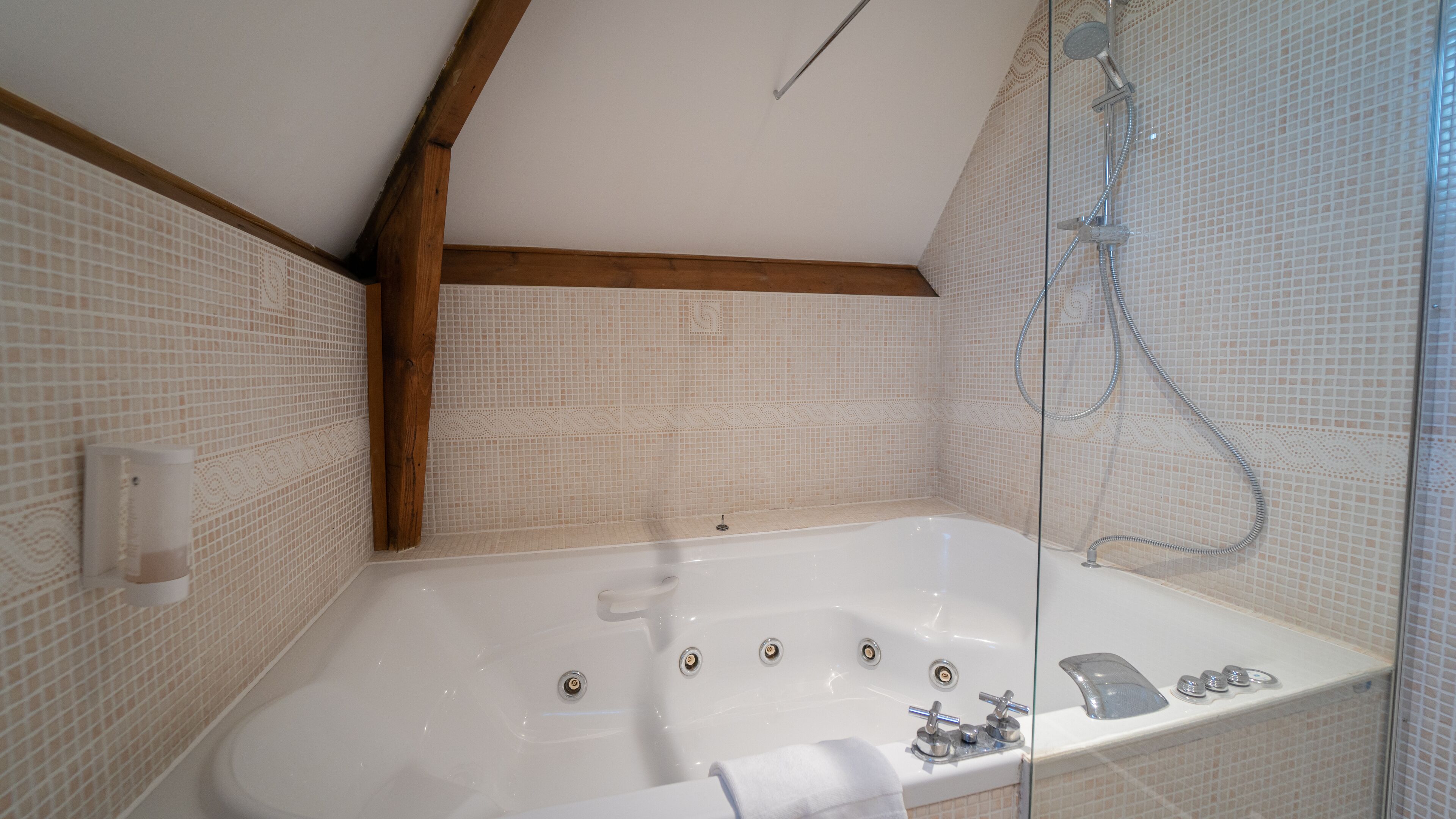 A bathroom with a freestanding bathtub, a glass-enclosed shower, and tiled walls with a wooden beam ceiling.