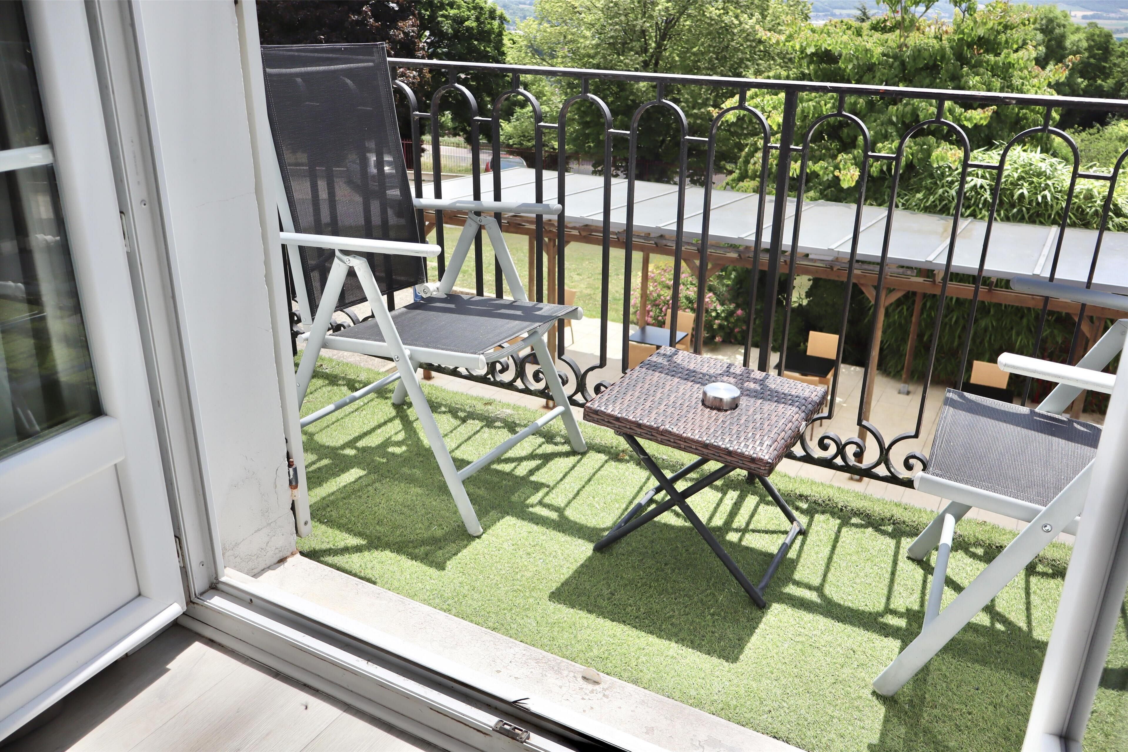 Un balcon avec une balustrade en métal, une petite table et deux chaises.