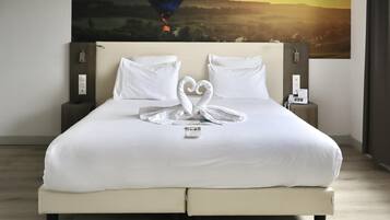 Un lit bien fait, avec du linge de lit blanc et une disposition de serviettes en forme de cœur. Un tableau représentant une montgolfière est accroché au mur derrière le lit.