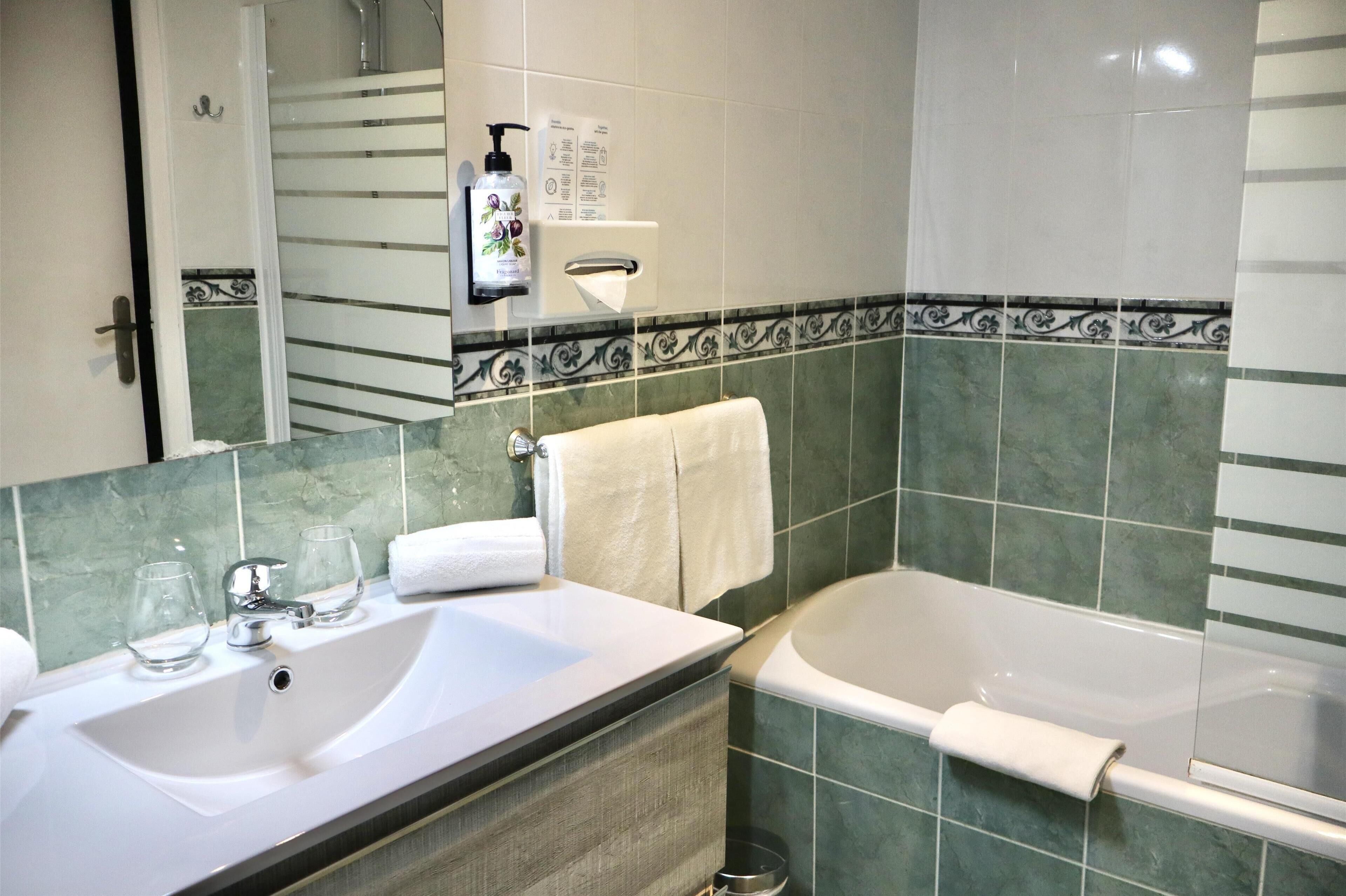 A bathroom with a sink, two glass tumblers, a towel, a bottle of shampoo, and a bathtub.