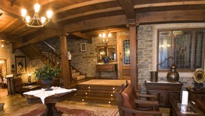A rustic interior with a stone fireplace, wooden staircase, and a chandelier.