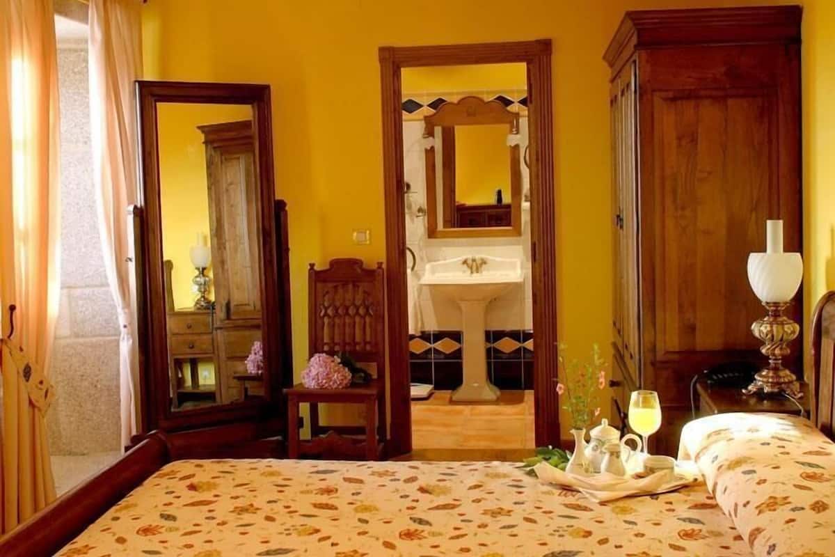 A room with a bed, a wooden wardrobe, a mirror, a sink, and a chair.