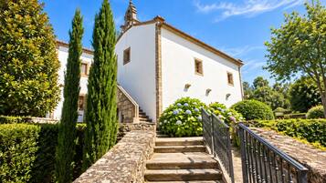 Un edificio blanco con una escalera de piedra que lleva a una puerta, rodeado de follaje y árboles.