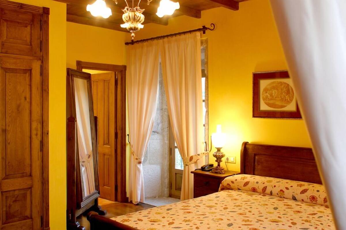 A room with a bed, a nightstand, a lamp, a framed picture on the wall, and a wooden door.