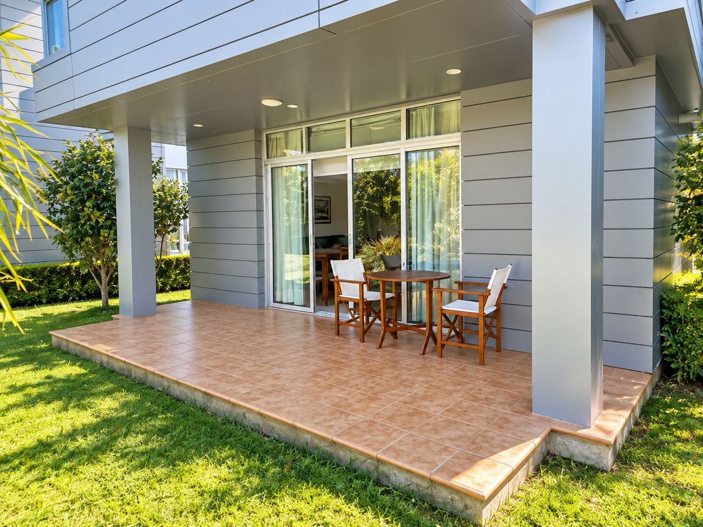 A covered patio area with a table and chairs, a sliding glass door leading to a room, and a well-maintained lawn.