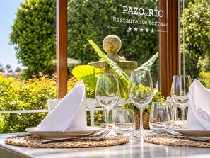 A table set for a meal with a view of a garden and a sign reading 'PAZO do RIO Restaurante Terrazza'. - Pazo do Río (Oleiros)