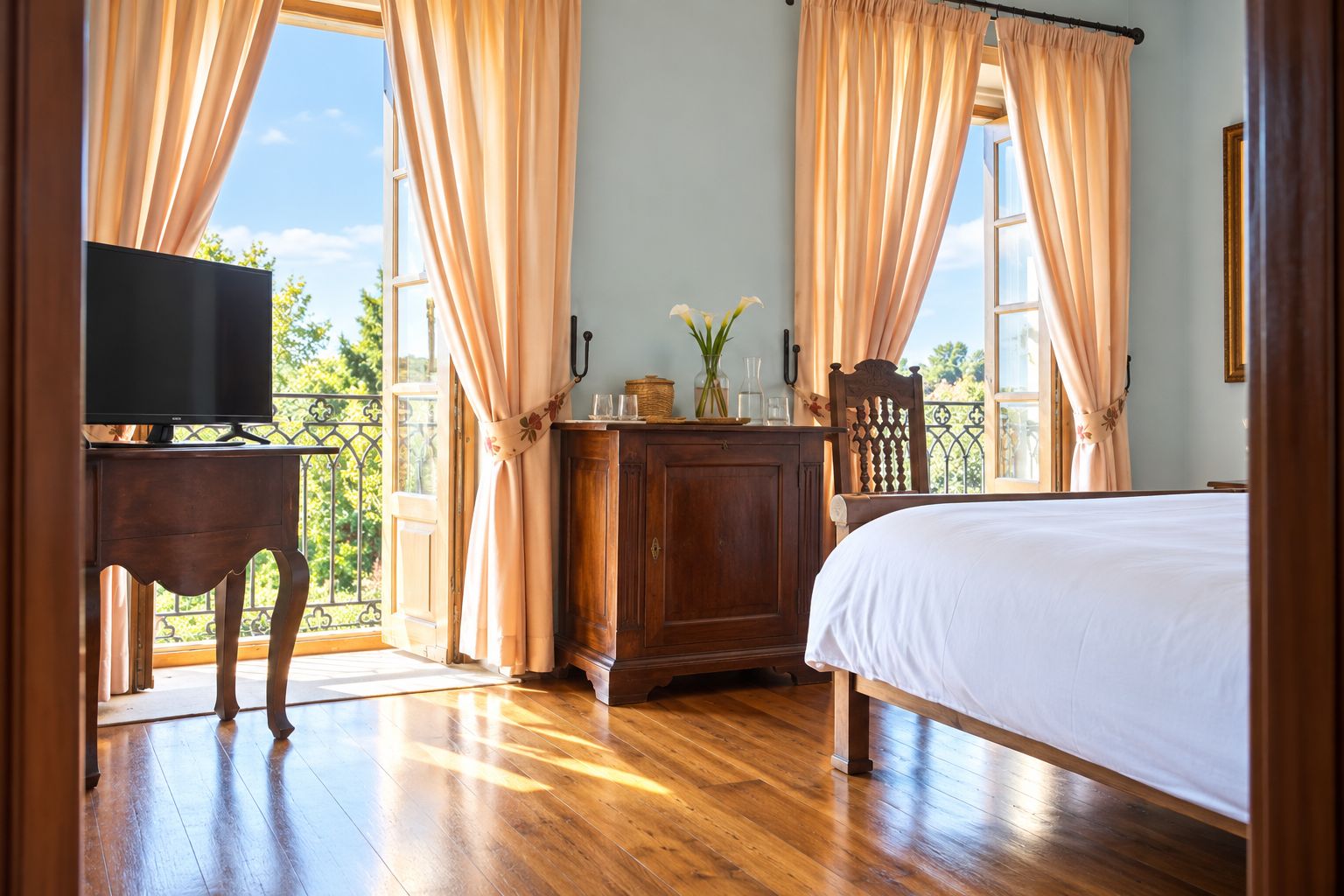 Habitación de hotel con cama, televisor sobre un soporte de madera, mueble de madera y vistas al exterior a través de amplias ventanas con cortinas.