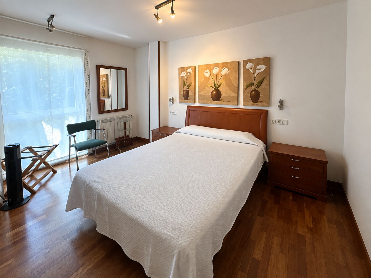 A bedroom with a large bed, a desk, a chair, and artwork on the wall.