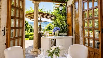 Un espacio de comedor al aire libre con una mesa dispuesta para dos, un pilar de piedra y una pérgola con vegetación.