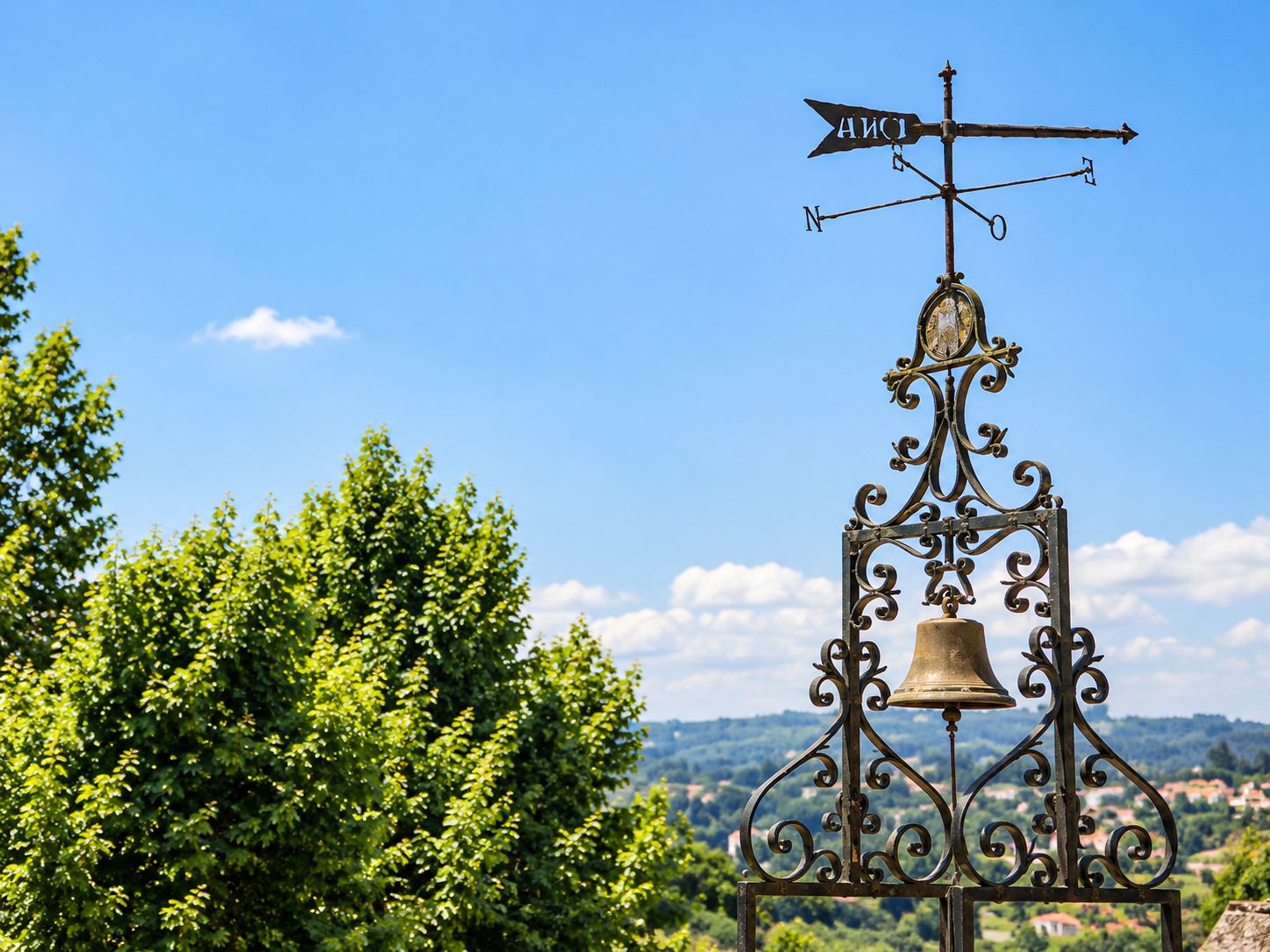 A weather vane with directional arrows and a bell on a metal structure.