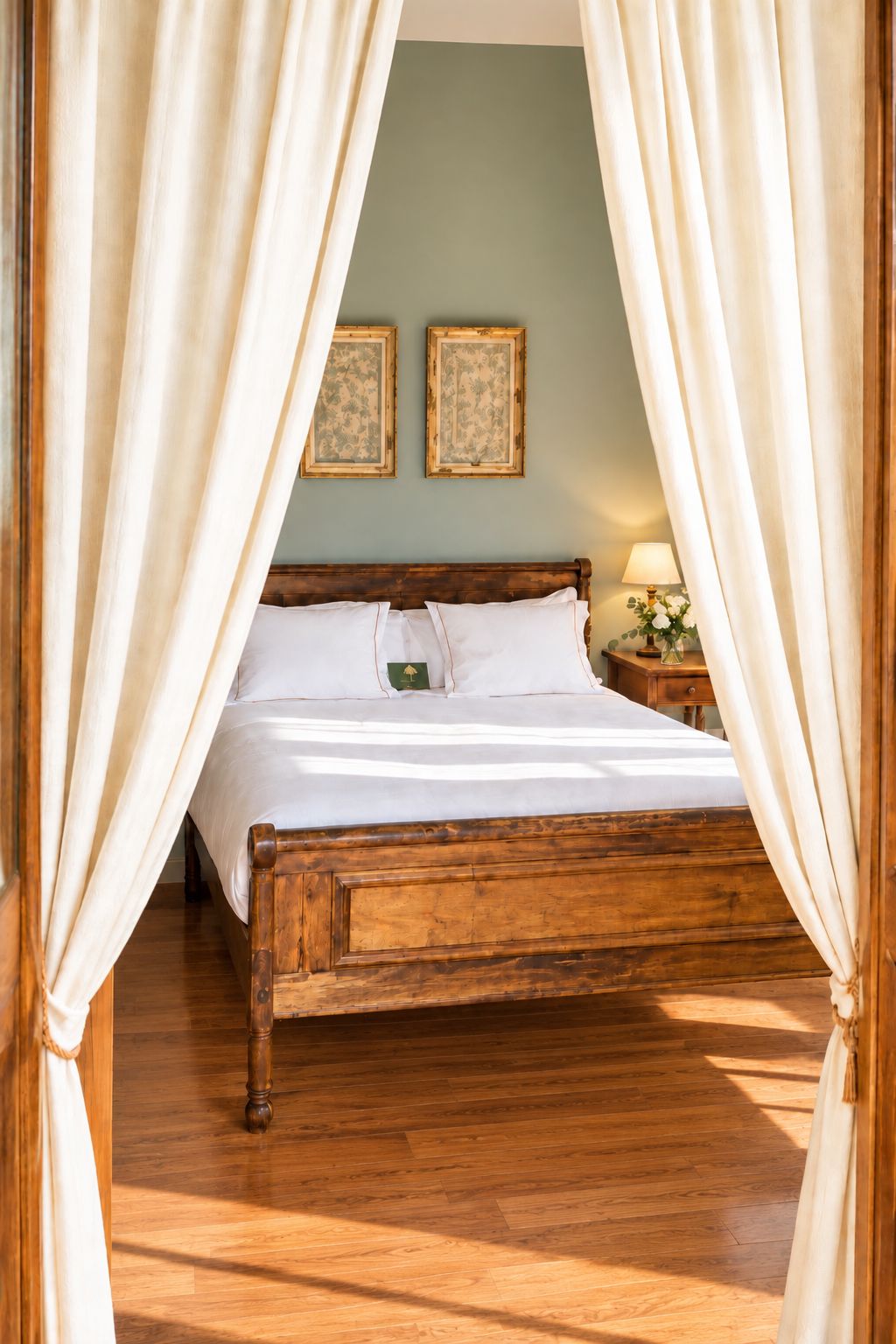 A wooden four-poster bed with white linens, a nightstand with a lamp, and two framed pictures on the wall.