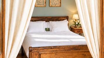 Una cama con dosel de madera con ropa blanca, una mesita de noche con lámpara y dos cuadros en la pared.