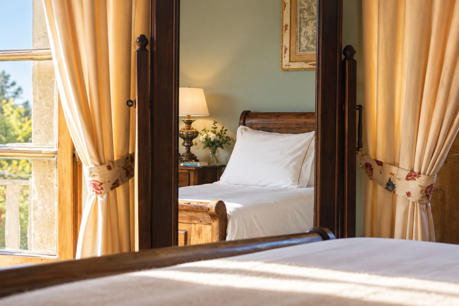 A bedroom with a wooden bed, a nightstand, a lamp, and a window with curtains.