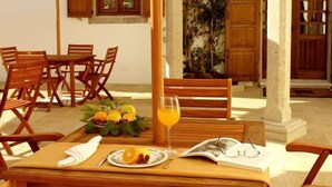 A wooden dining table with chairs, a glass of orange juice, a plate with fruit, and an open magazine.