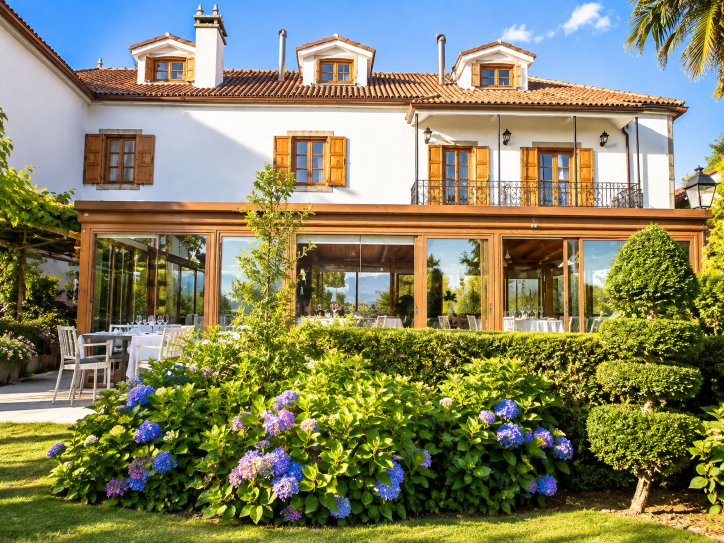 A two-story building with a balcony, large windows, and a garden with hydrangeas.