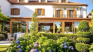 A two-story building with a balcony, large windows, and a garden with hydrangeas.