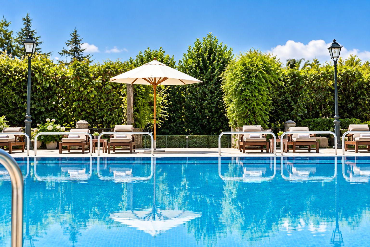 A swimming pool with lounge chairs and umbrellas, surrounded by greenery and trees.