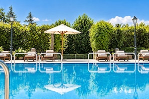 En swimmingpool med solstolar och parasoller, omgiven av grönska och träd.