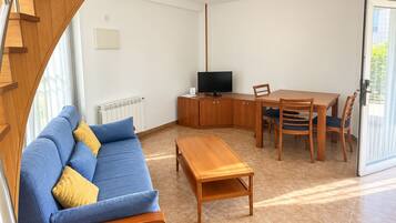 Een moderne woonkamer met een bank, een houten salontafel, een televisie en een eethoek met stoelen en een tafel.