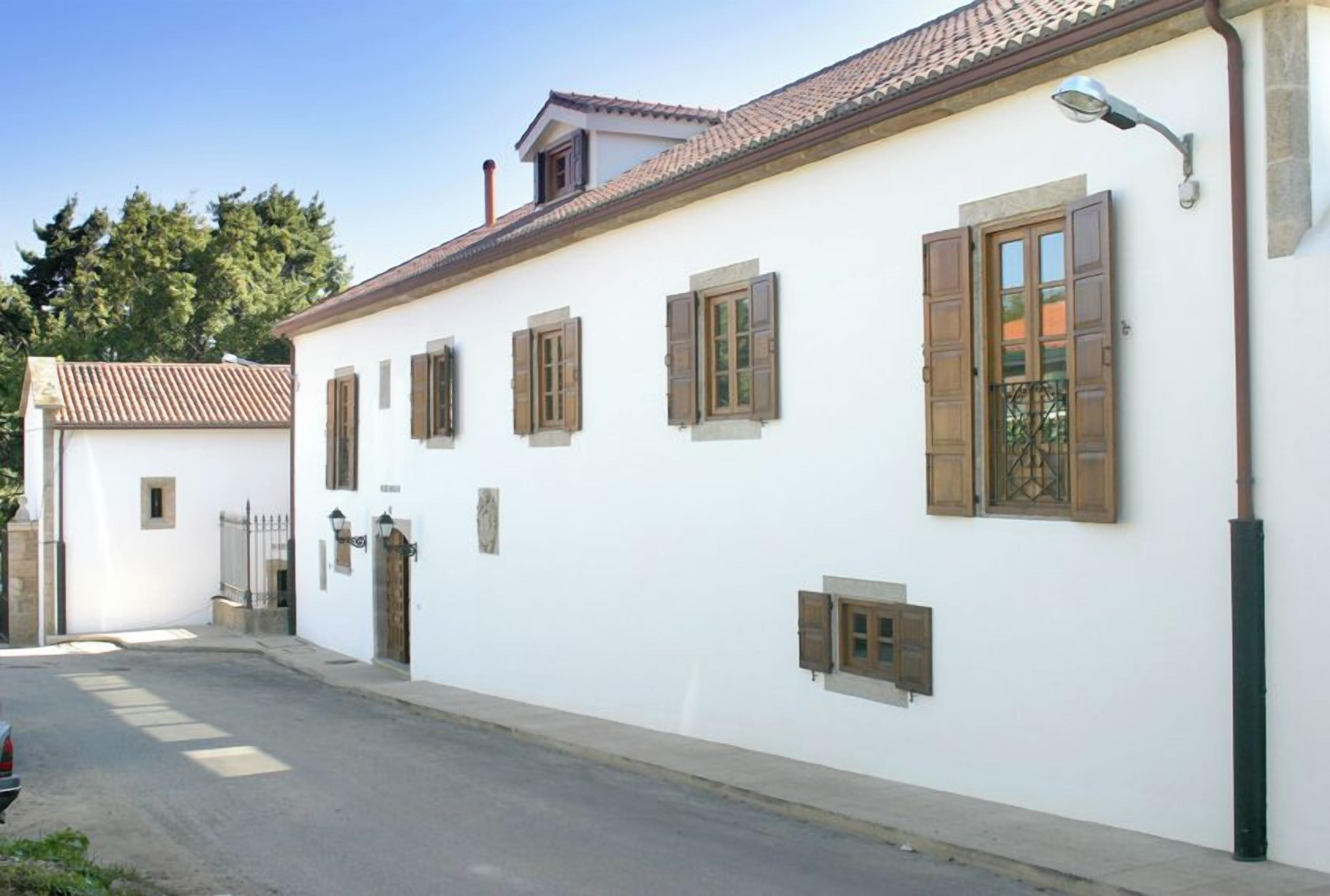 A white building with a tiled roof, wooden shutters, and a street lamp.