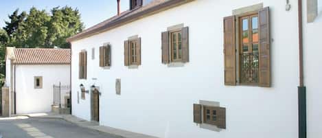 A white building with a tiled roof, wooden shutters, and a street lamp.