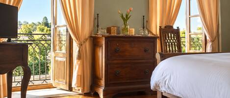 A bedroom with a wooden dresser, a bed, and a view of a balcony.