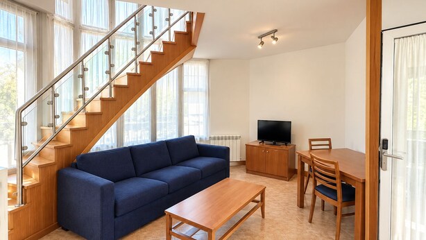 Un salon moderne avec un escalier en bois, un canapé bleu, une table basse en bois, un téléviseur posé sur un meuble et un coin repas avec une table et des chaises.
