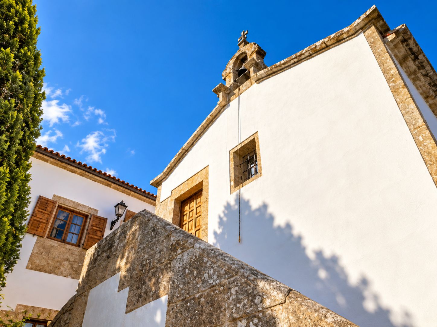 Un edificio con fachada blanca, una escalera de piedra y un ventanal pequeño.