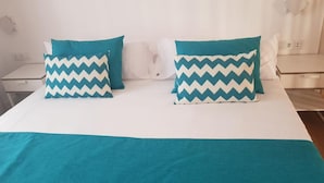 Un llit amb dos coixins de disseny en zigzag, un panell frontal blanc i un llençol color turquesa.