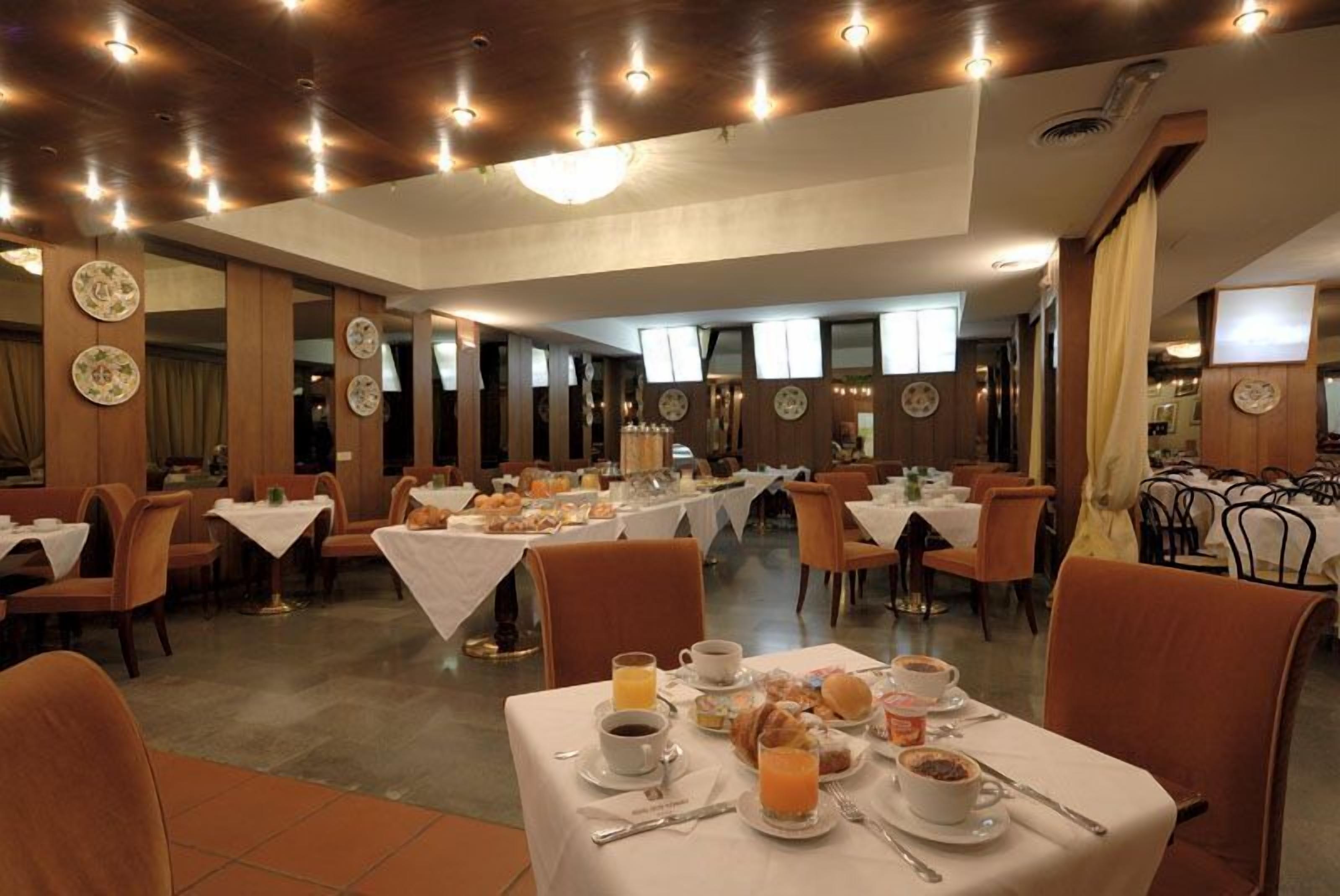 Un comedor con mesas dispuestas para el desayuno, con platos, tazas y cubiertos.