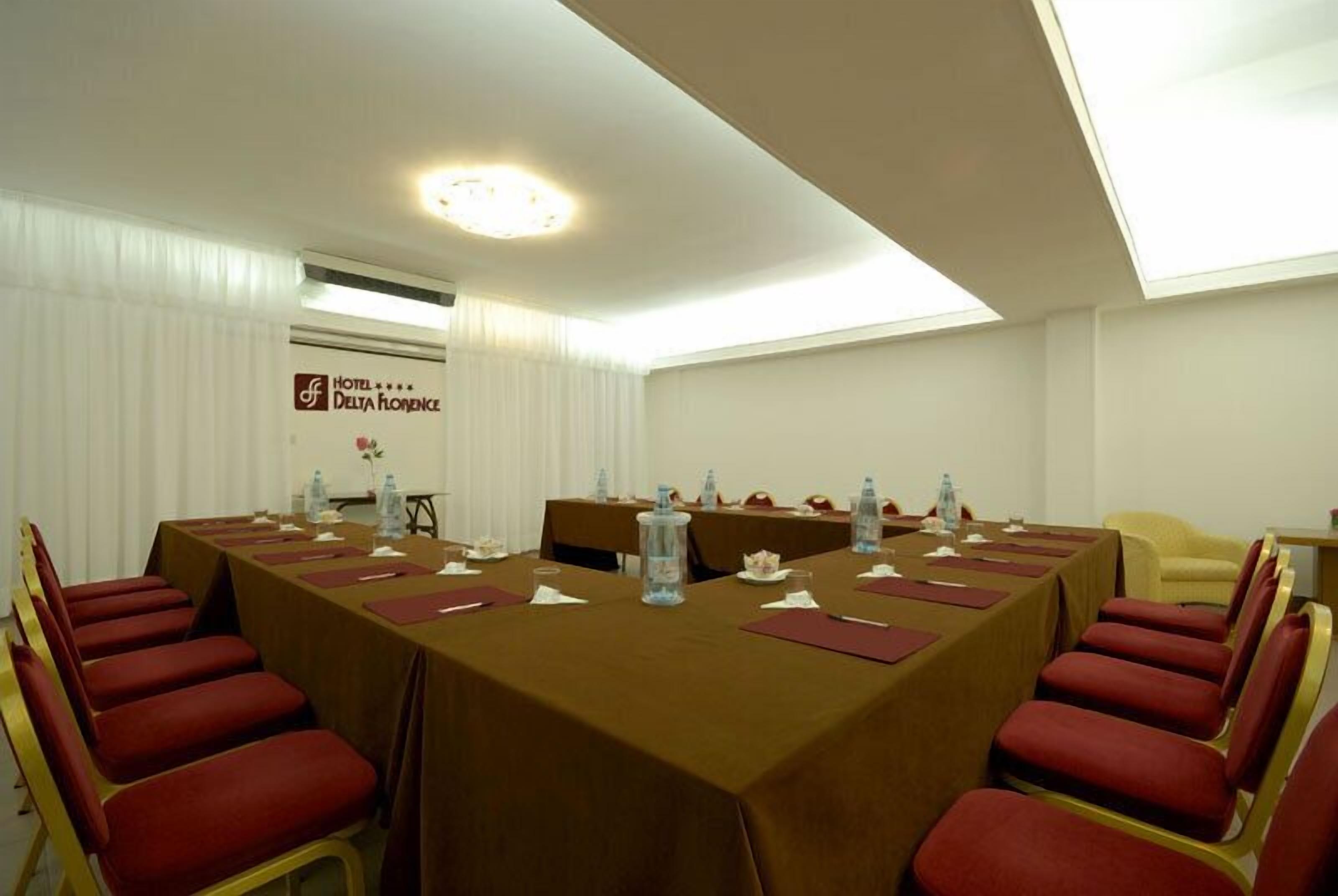 A conference room with a long table, red chairs, and a sign for Hotel Delta Florence.