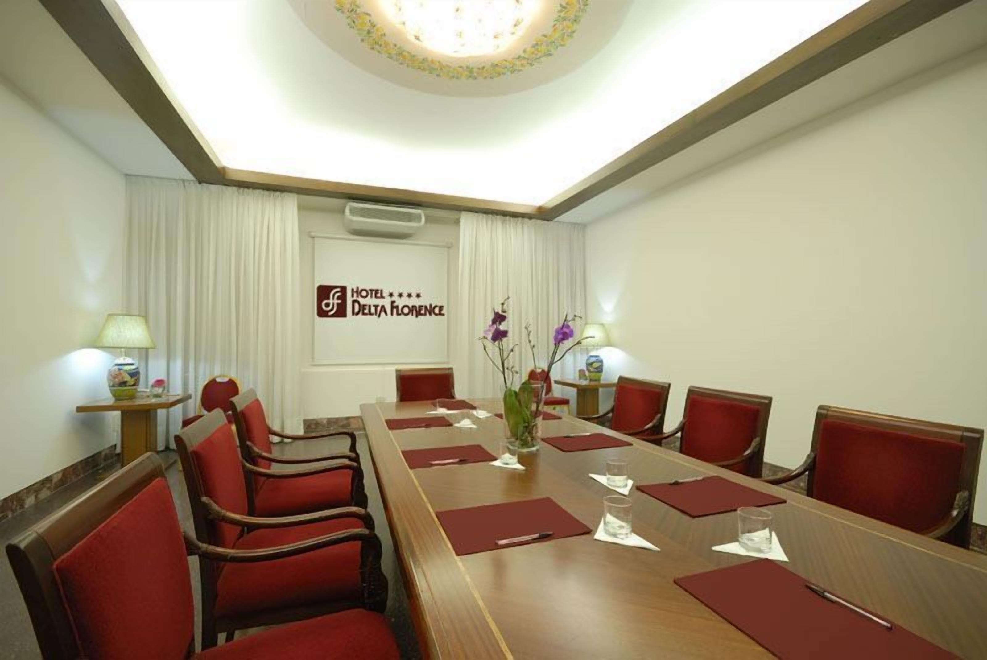 A conference room with a long table, red chairs, and a logo for Hotel Delta Florence.