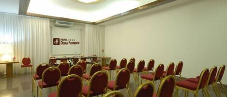 A conference room with rows of red chairs and a table, a whiteboard, and a sign for Hotel Delta Florence.