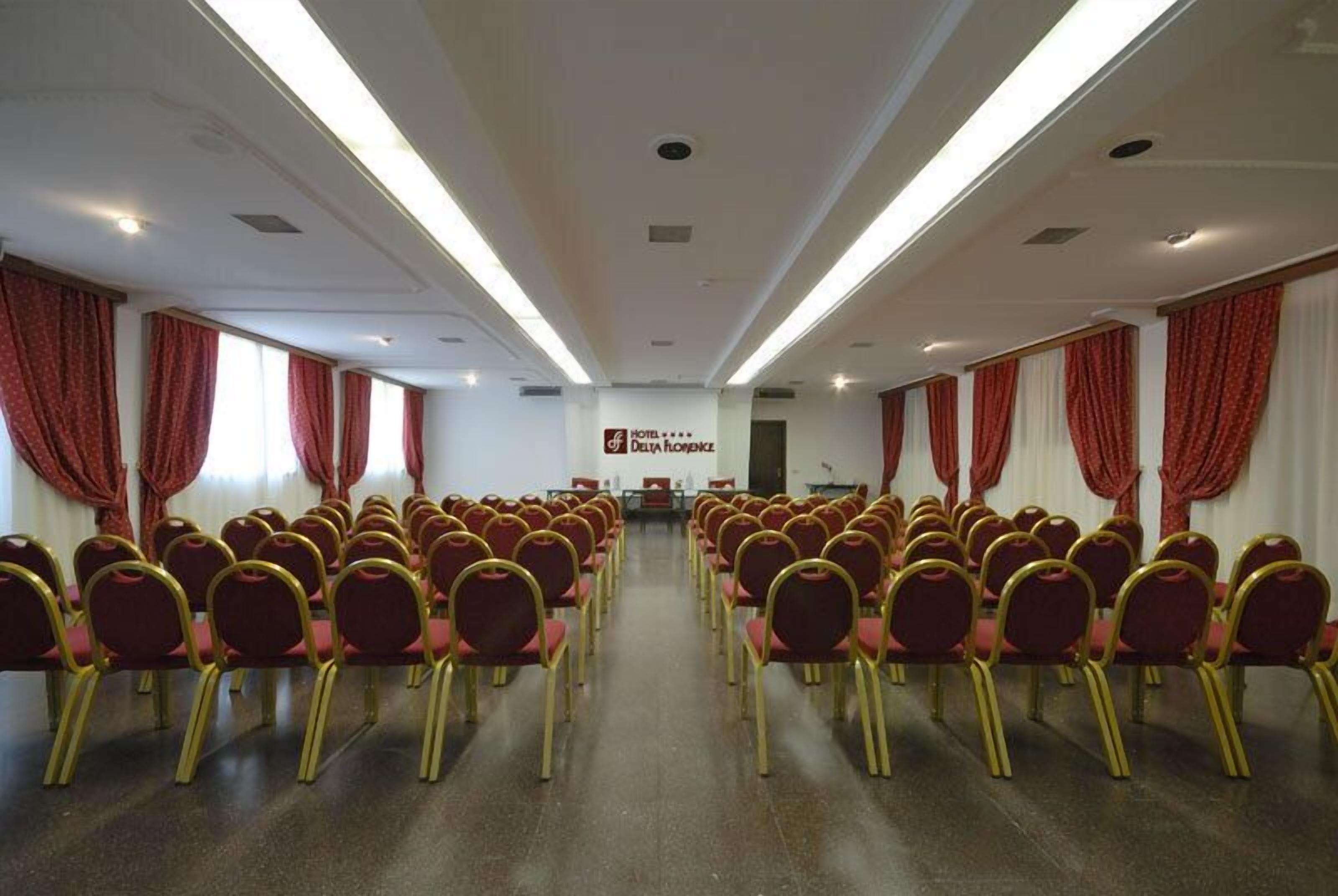 A conference room with rows of chairs, a podium, and a banner reading "Hotel de Draga Resort".