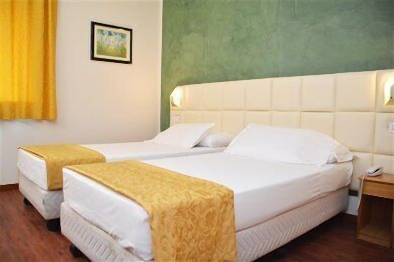 A hotel room with two single beds, a green accent wall, a framed picture, and a bedside table with a phone.