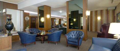 Un vestíbulo de hotel con sofás de cuero azul, un mostrador de recepción de madera y un espejo grande que refleja la sala.
