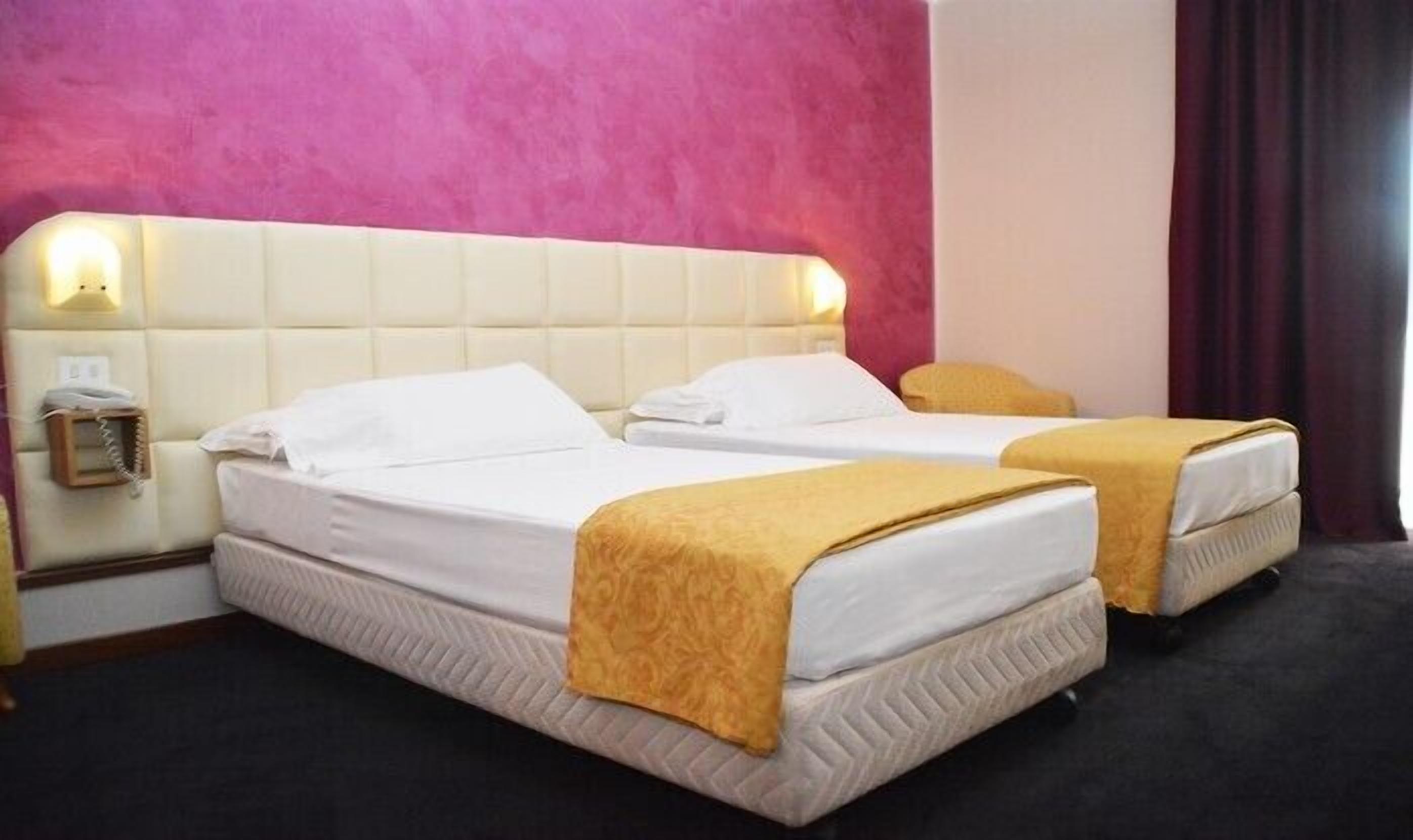 Une chambre d’hôtel avec deux lits, un mur rose et un téléphone sur la table de chevet.