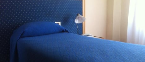 A bed with a blue bedspread and pillows, a bedside lamp, and a phone on the nightstand.