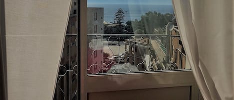Una habitación con un ventanal amplio, una cama con colcha rosa y vistas a edificios y una masa de agua.