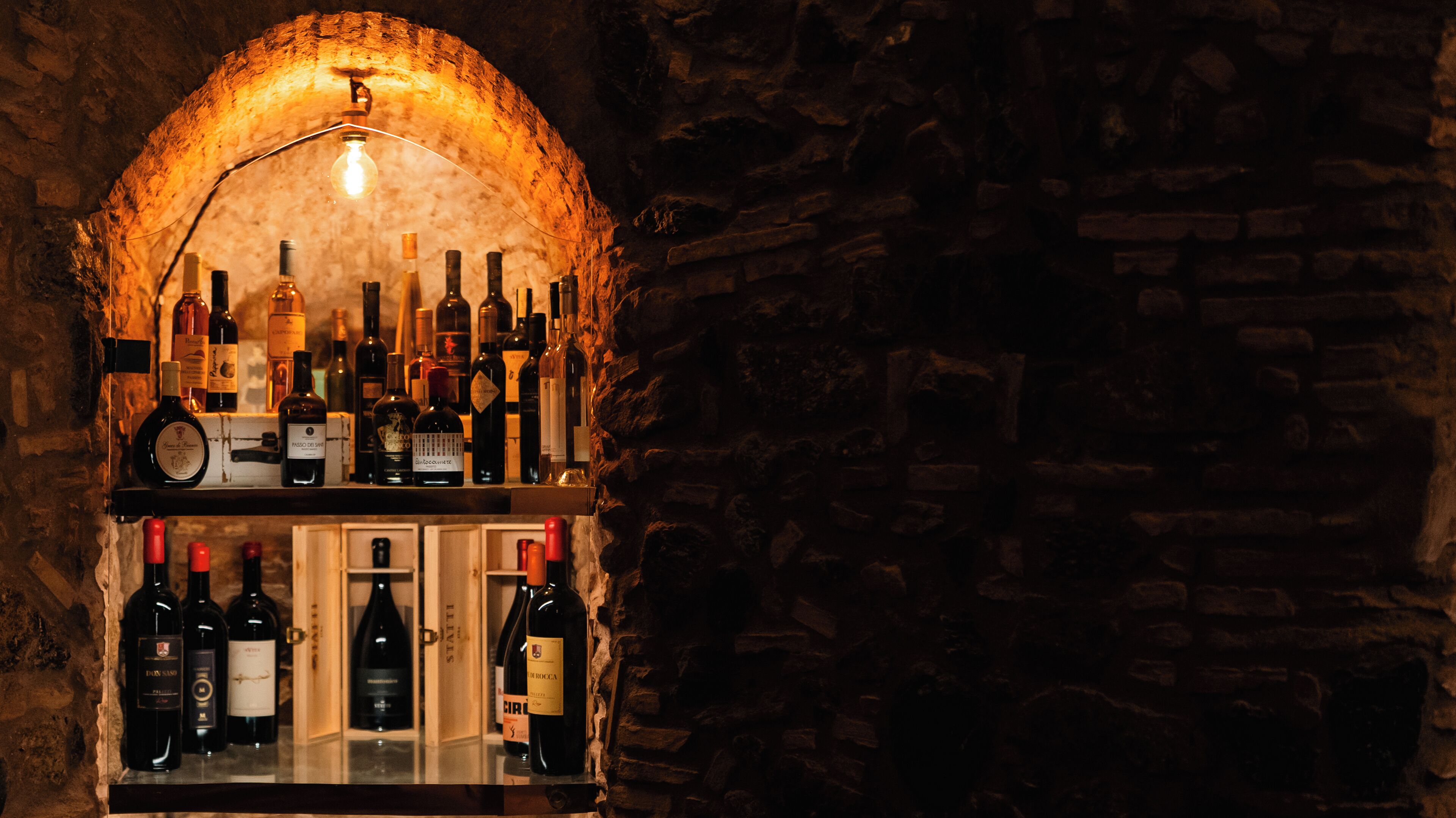 A wine rack with various bottles against a stone wall backdrop.