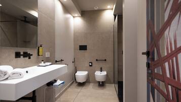 Une salle de bain moderne avec un lavabo blanc, deux toilettes, une douche et une porte en verre.