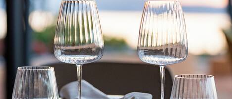 Una mesa servida con cuatro copas de vino y platos, con vista al agua de fondo.