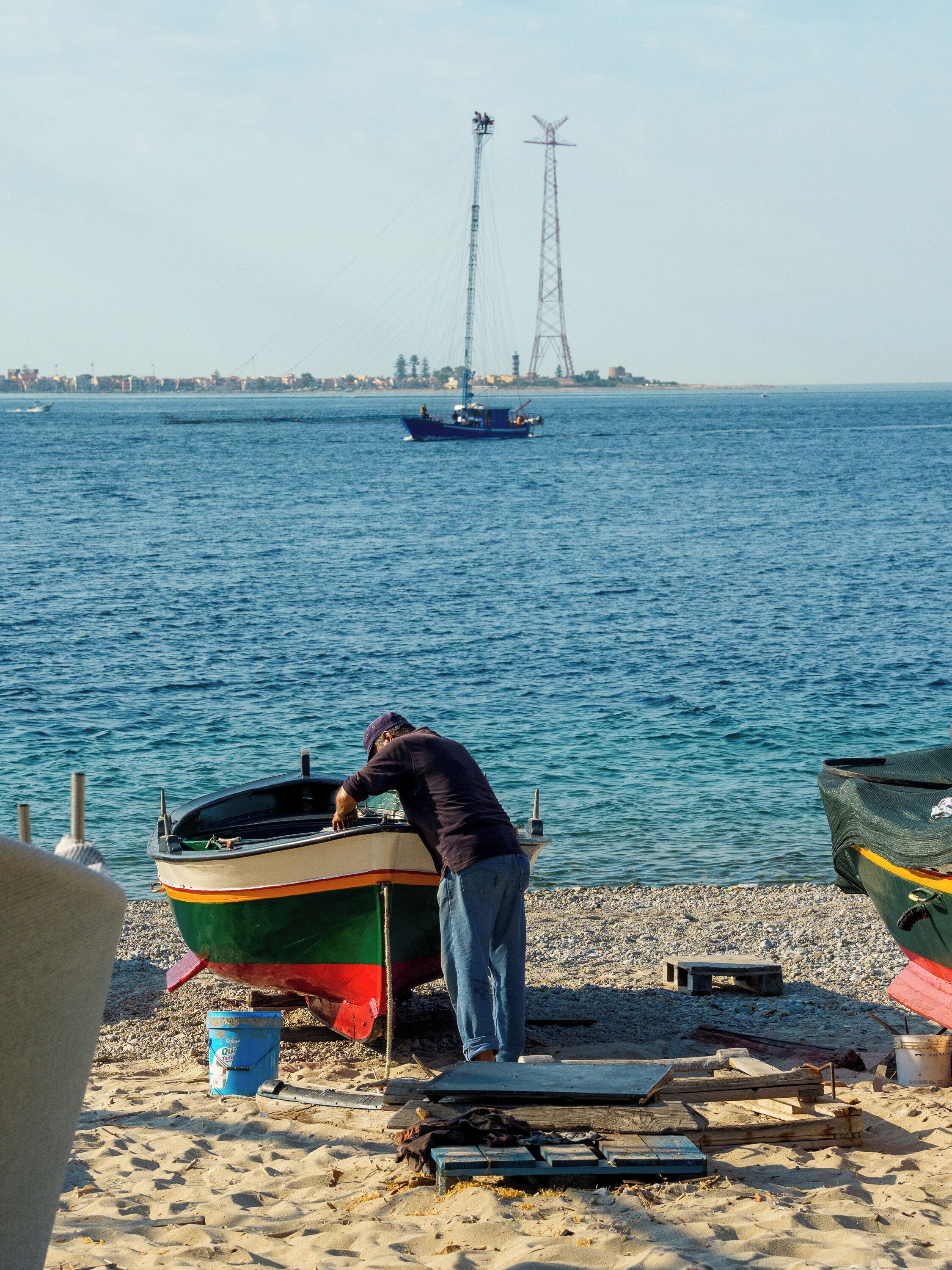Una playa con barcos, una persona cerca de un bote y una vista distante de un horizonte urbano.
