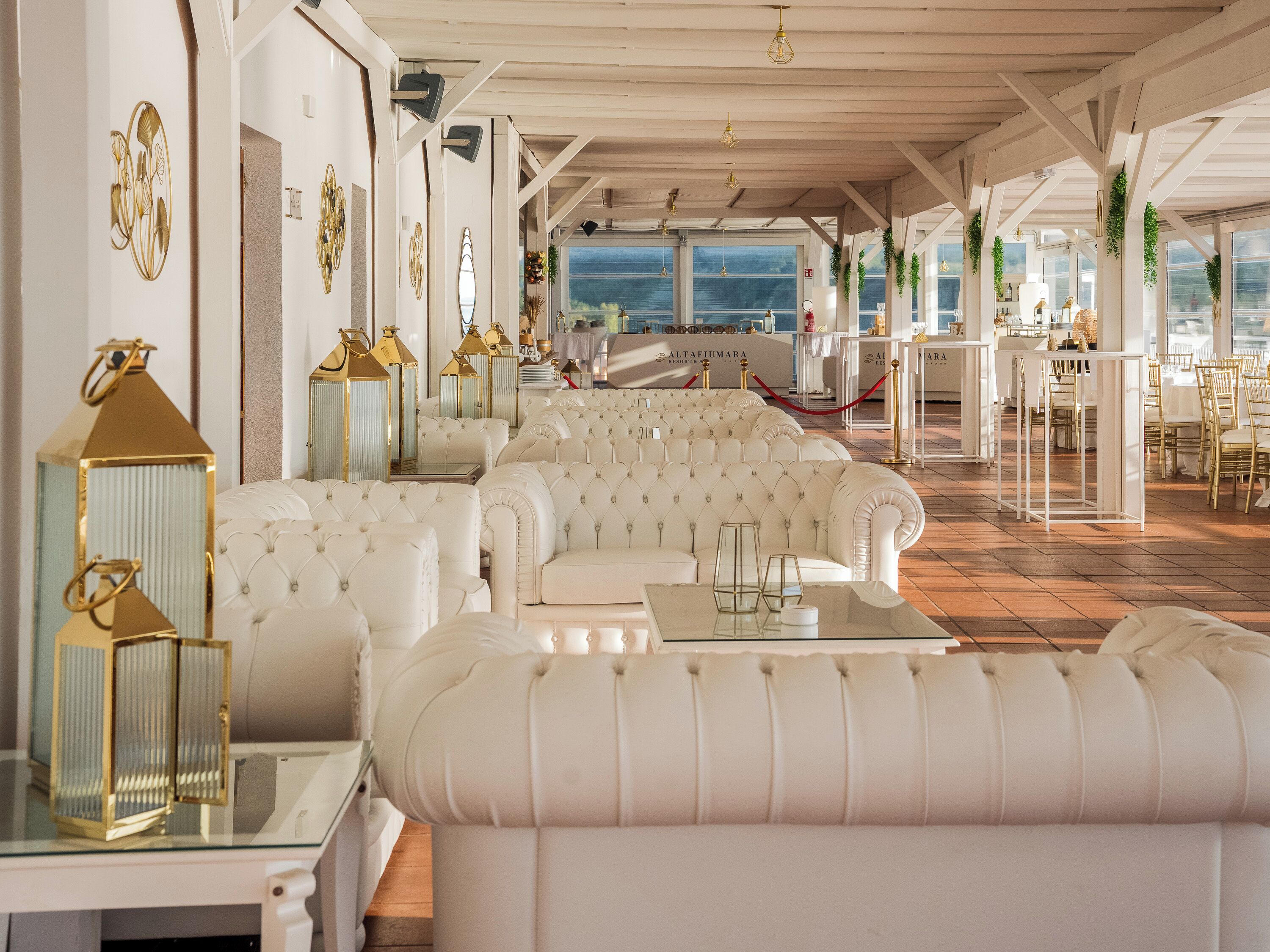 A luxurious hotel lobby with white leather sofas, gold-framed wall art, and a view of the sea.
